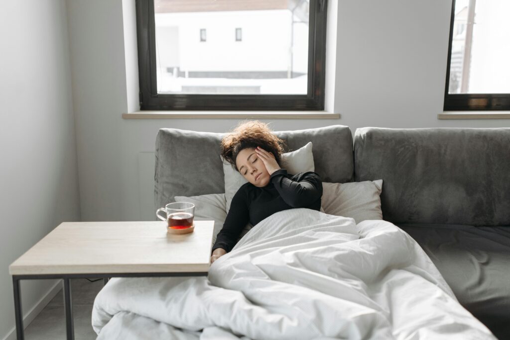 A woman rests on a couch indoors, feeling unwell, with a cup of tea nearby.